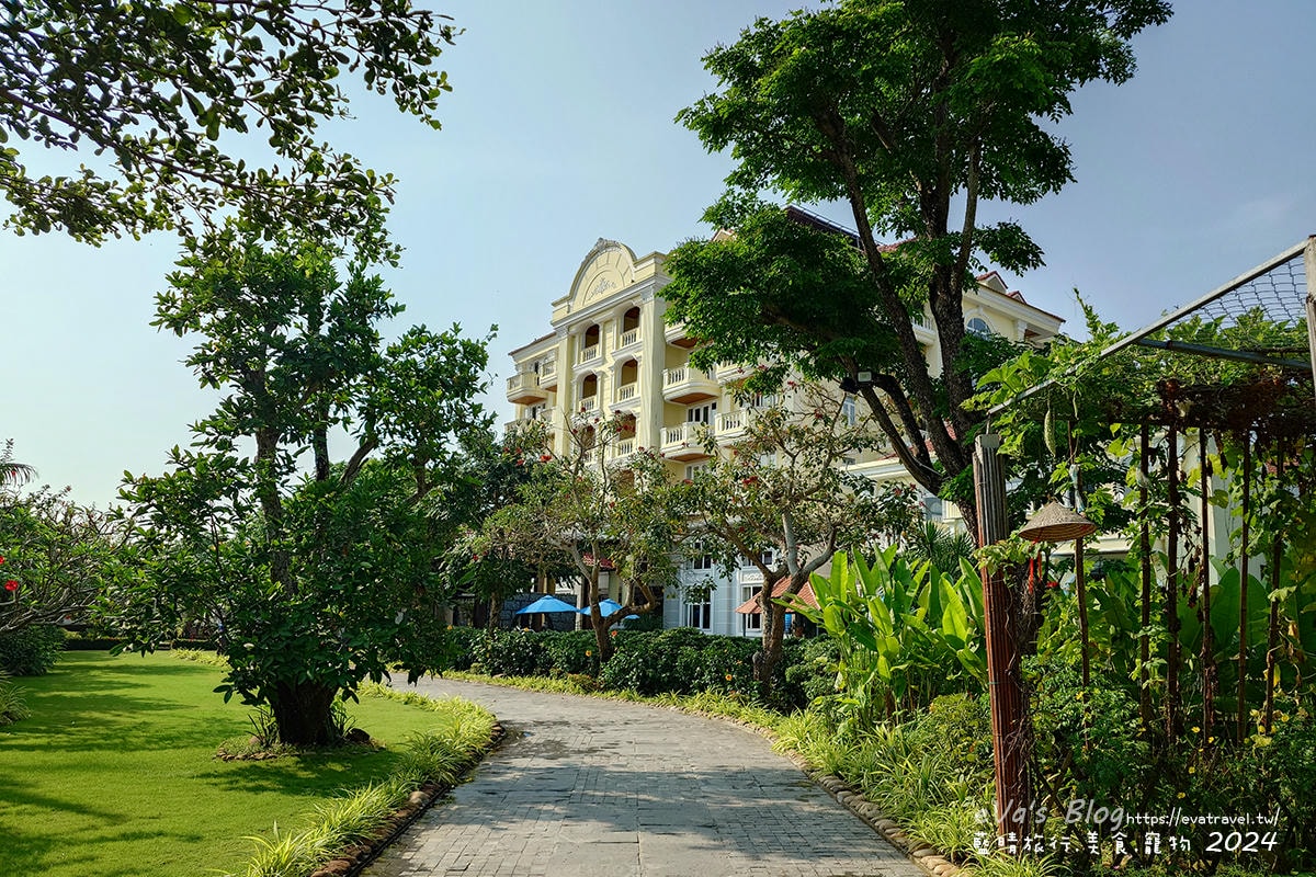 通往 Le Pavillon Hoi An 主建築的步行小徑，遠處可見鵝黃色外牆